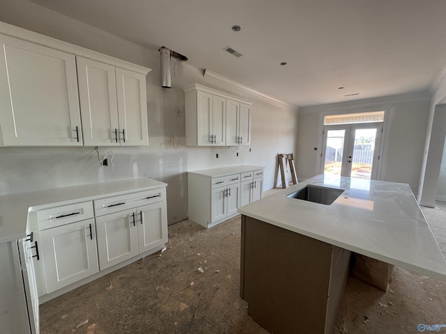 kitchen with french doors, crown molding, a kitchen island with sink, and white cabinets
