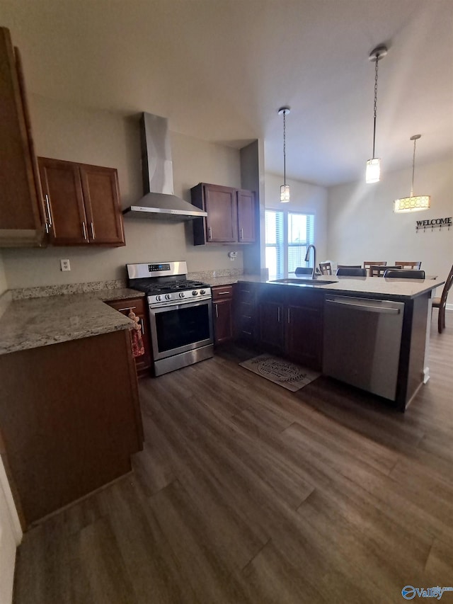 kitchen with dark wood-type flooring, appliances with stainless steel finishes, a peninsula, wall chimney exhaust hood, and a sink