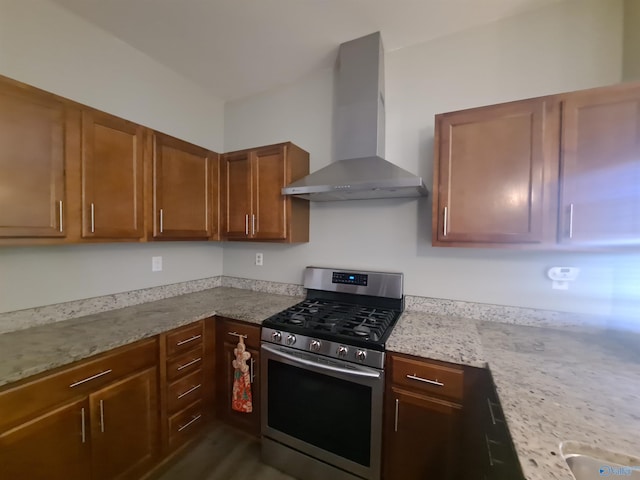 kitchen featuring brown cabinetry, wall chimney range hood, light stone counters, and gas stove