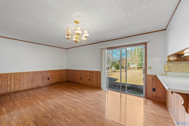 unfurnished dining area featuring a notable chandelier, a textured ceiling, wooden walls, and light hardwood / wood-style flooring