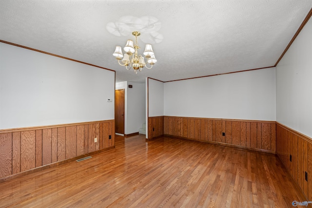 empty room with a textured ceiling, an inviting chandelier, and light hardwood / wood-style flooring