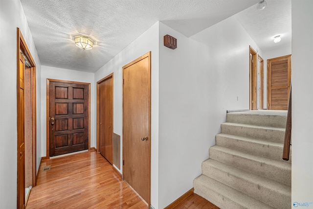 hallway with a textured ceiling and light hardwood / wood-style floors