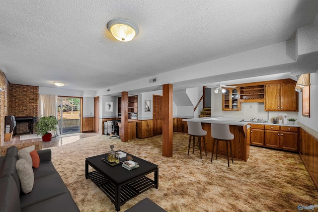 living room with a textured ceiling, wood walls, light carpet, and a brick fireplace