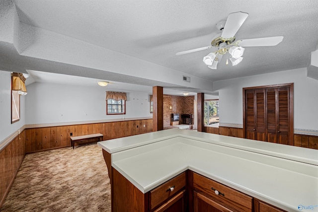 kitchen with kitchen peninsula, a textured ceiling, light colored carpet, wooden walls, and a fireplace