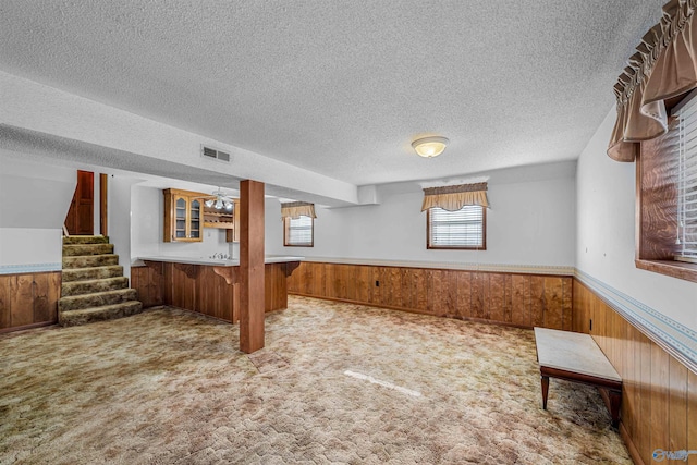 basement with wood walls, light colored carpet, and a textured ceiling