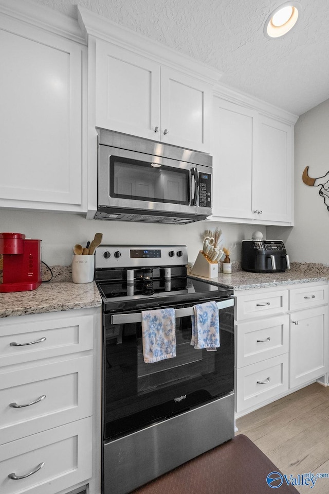 713 Rabbittown Rd, Glencoe, AL 35905 - kitchen featuring appliances with stainless steel finishes, a textured ceiling, white cabinets, light wood finished floors, and light stone counters