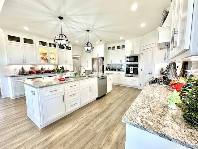 kitchen featuring an island with sink, white cabinets, hanging light fixtures, and stainless steel appliances