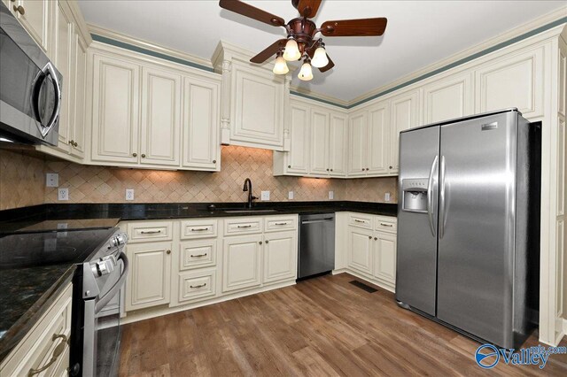 kitchen with appliances with stainless steel finishes, sink, backsplash, cream cabinets, and dark wood-type flooring