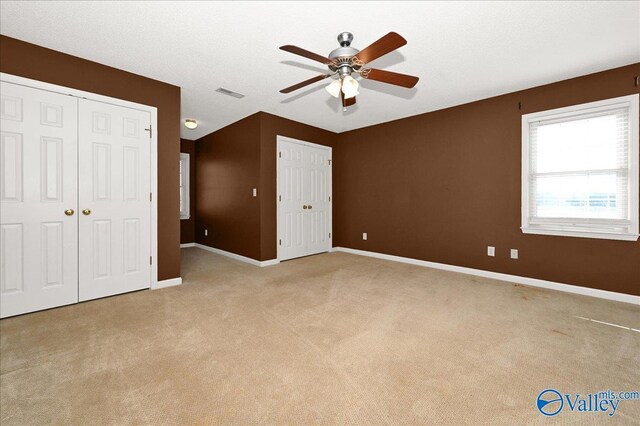 unfurnished bedroom featuring two closets, light colored carpet, and ceiling fan