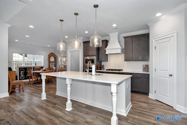 kitchen featuring custom range hood, dark brown cabinets, a kitchen island with sink, sink, and dark hardwood / wood-style floors