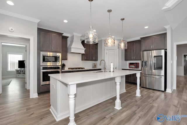 kitchen featuring appliances with stainless steel finishes, dark brown cabinetry, a center island with sink, and custom range hood