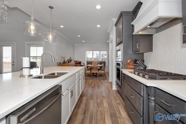 kitchen with sink, ornamental molding, custom range hood, white cabinetry, and stainless steel appliances