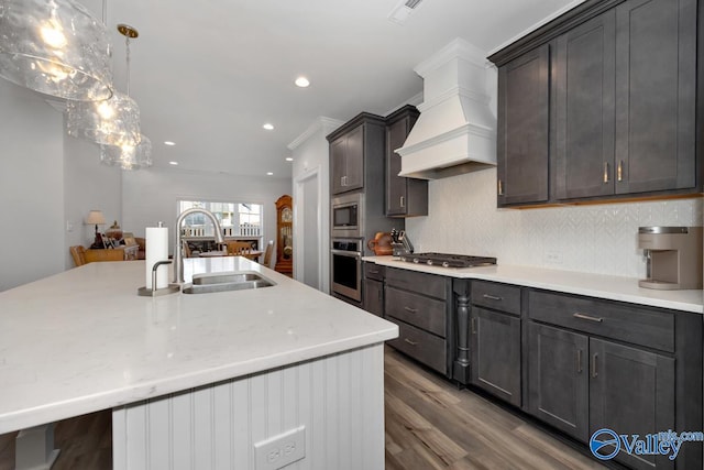 kitchen with appliances with stainless steel finishes, custom range hood, sink, hardwood / wood-style flooring, and hanging light fixtures