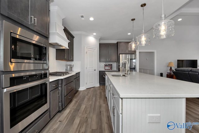 kitchen with decorative light fixtures, dark wood-type flooring, an island with sink, and stainless steel appliances