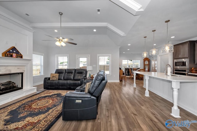 living room with ornamental molding, vaulted ceiling, ceiling fan, a premium fireplace, and hardwood / wood-style floors