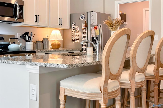 kitchen with white cabinetry, a breakfast bar area, stainless steel appliances, and light stone counters