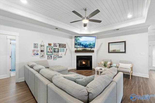 living room featuring a large fireplace, baseboards, dark wood finished floors, ornamental molding, and a tray ceiling