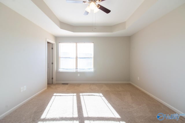 carpeted spare room with a tray ceiling and ceiling fan