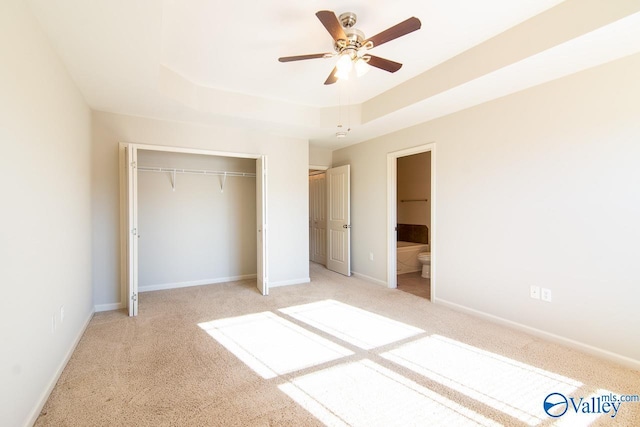 unfurnished bedroom with light colored carpet, a raised ceiling, a closet, and ceiling fan