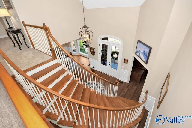 stairway with an inviting chandelier, a high ceiling, french doors, and wood finished floors
