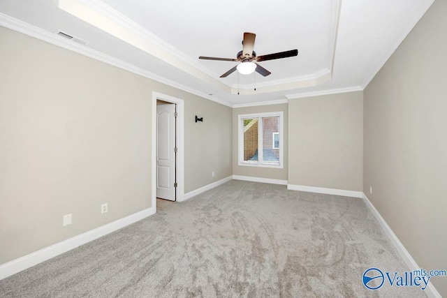 carpeted spare room with ceiling fan, visible vents, ornamental molding, and a raised ceiling