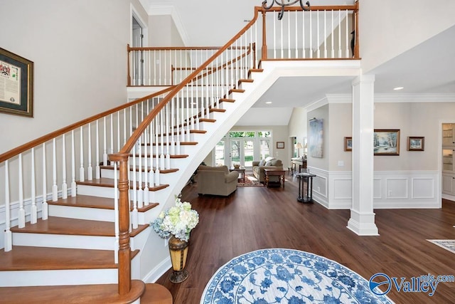 staircase with decorative columns, a towering ceiling, crown molding, wood finished floors, and recessed lighting