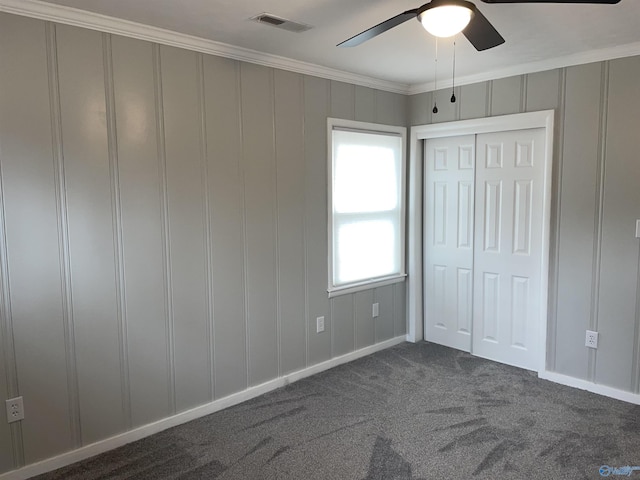 unfurnished bedroom with crown molding, a closet, ceiling fan, and dark colored carpet