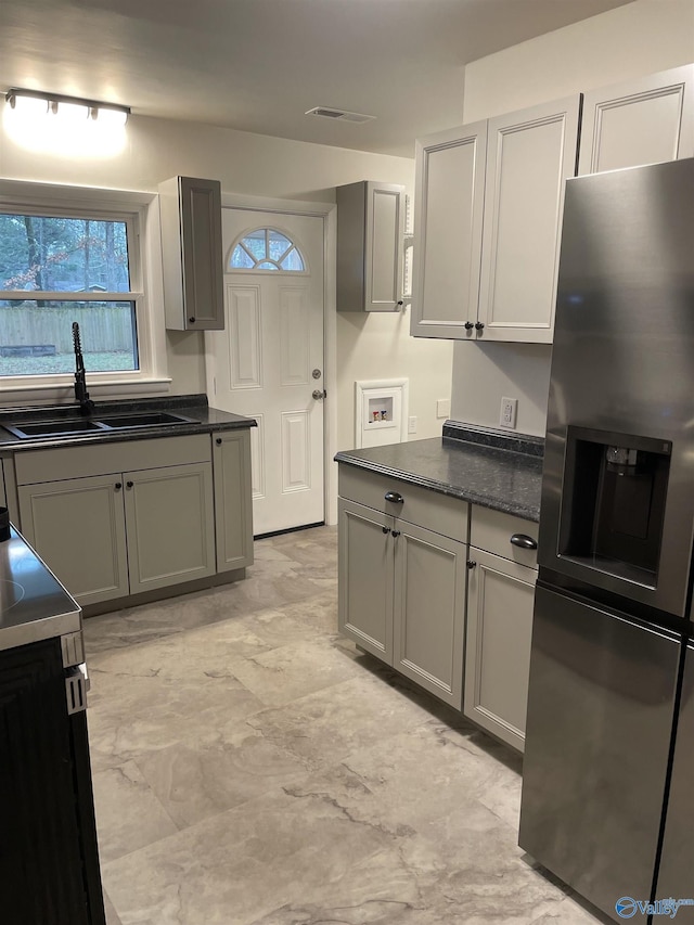 kitchen with gray cabinetry, sink, stainless steel fridge, and dark stone counters