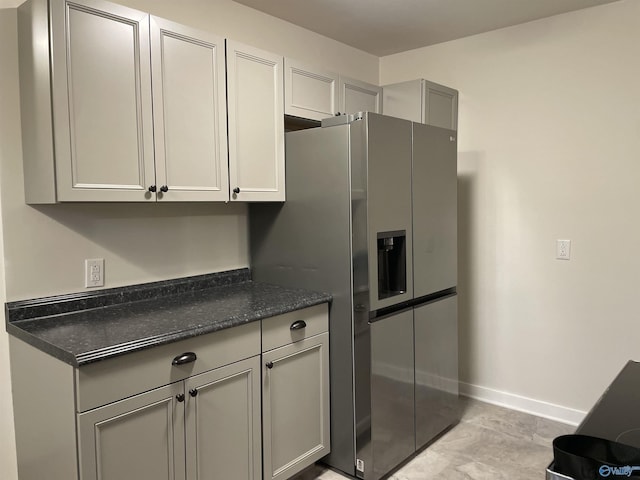 kitchen featuring stainless steel refrigerator with ice dispenser, dark stone countertops, and gray cabinetry