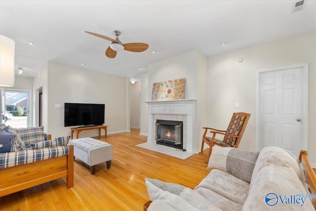 living room with light wood-type flooring, a tiled fireplace, and ceiling fan