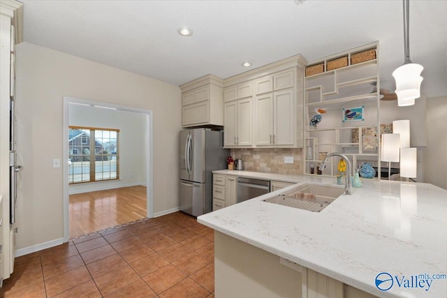 kitchen with stainless steel appliances, kitchen peninsula, pendant lighting, sink, and backsplash