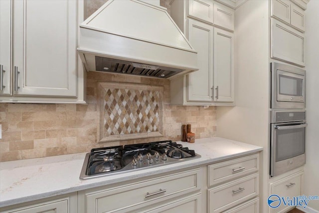 kitchen featuring custom exhaust hood, light stone counters, decorative backsplash, and stainless steel appliances