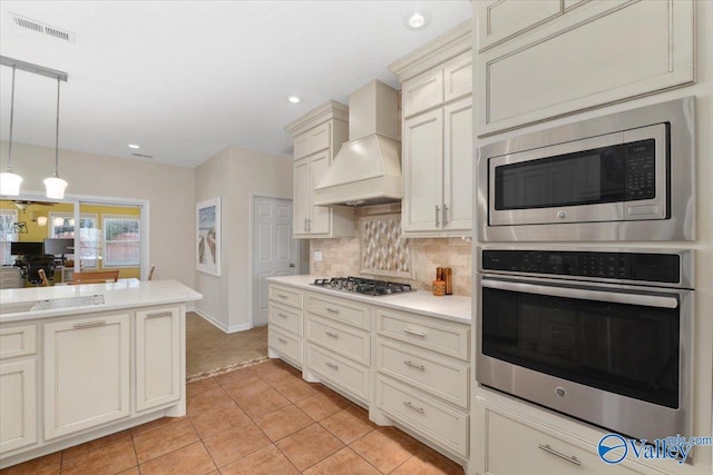 kitchen with decorative light fixtures, light tile patterned floors, decorative backsplash, premium range hood, and appliances with stainless steel finishes