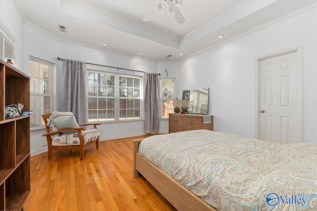 bedroom with crown molding, ceiling fan, a tray ceiling, and light wood-type flooring