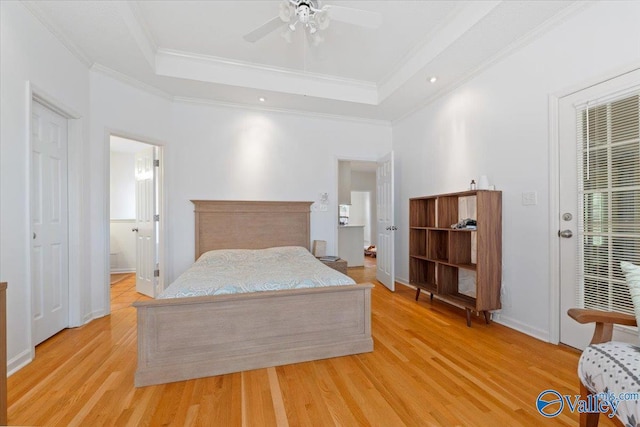 bedroom with connected bathroom, light wood-type flooring, ceiling fan, a tray ceiling, and ornamental molding