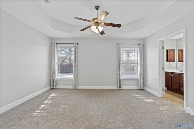 carpeted spare room featuring a raised ceiling, ceiling fan, and a wealth of natural light