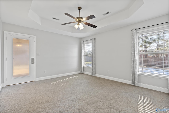 carpeted empty room featuring ceiling fan and a raised ceiling