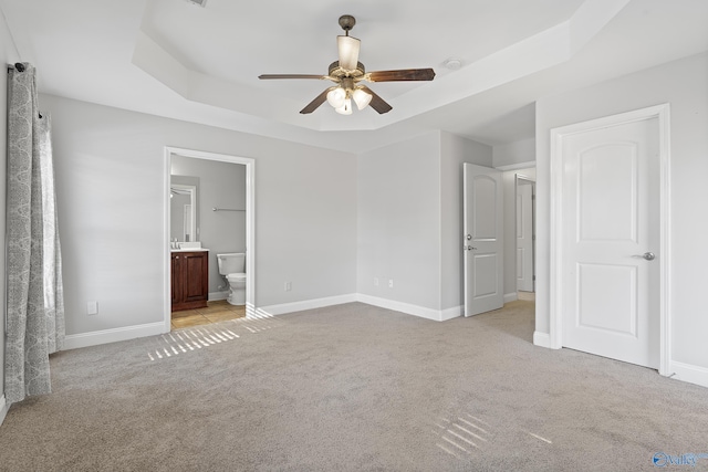 unfurnished bedroom with light carpet, ceiling fan, connected bathroom, and a tray ceiling