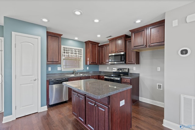 kitchen featuring appliances with stainless steel finishes, dark hardwood / wood-style floors, dark stone counters, a kitchen island, and sink