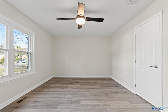 empty room with ceiling fan, light wood finished floors, visible vents, and baseboards