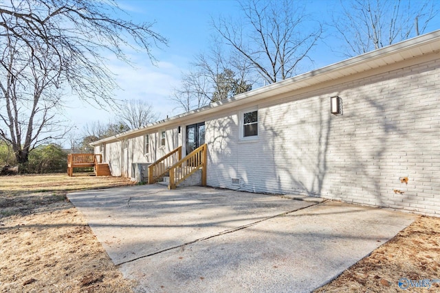 view of side of property with brick siding, a patio, crawl space, a deck, and driveway