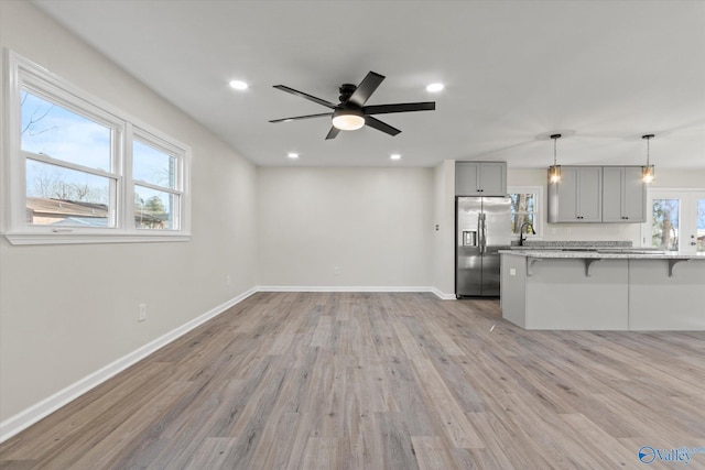 kitchen with gray cabinets, a kitchen breakfast bar, light wood-type flooring, stainless steel fridge, and baseboards