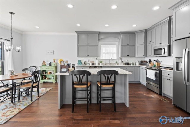 kitchen with pendant lighting, a center island, light stone counters, stainless steel appliances, and crown molding