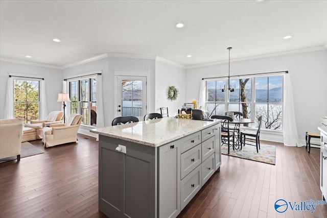 kitchen featuring crown molding, hanging light fixtures, dark hardwood / wood-style flooring, a kitchen island, and light stone countertops