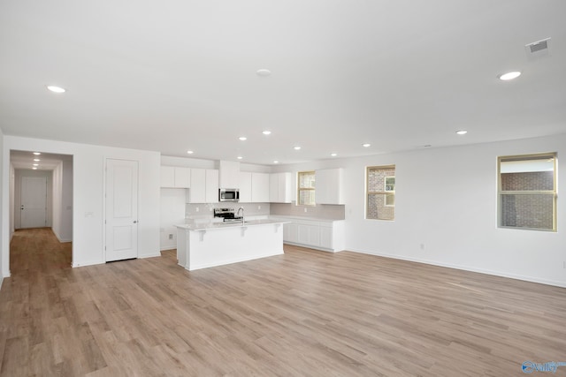 kitchen with stainless steel appliances, an island with sink, white cabinets, a kitchen bar, and light wood-type flooring