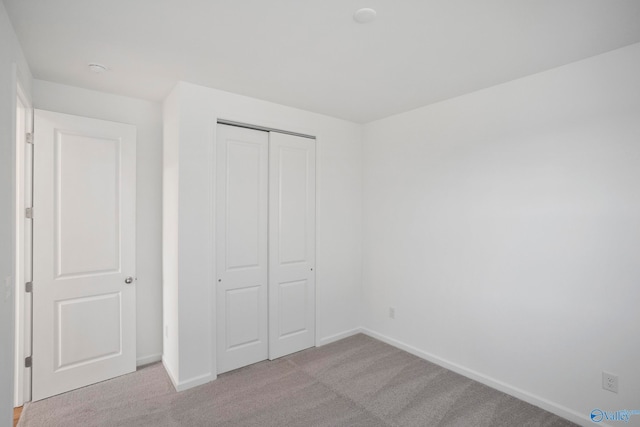 unfurnished bedroom with light colored carpet and a closet