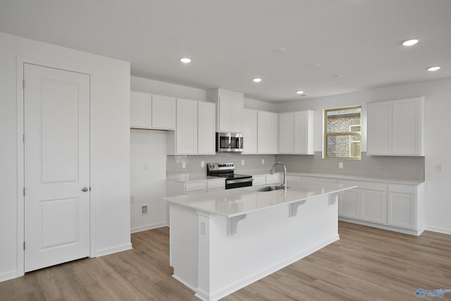 kitchen with white cabinetry, appliances with stainless steel finishes, sink, and a center island with sink