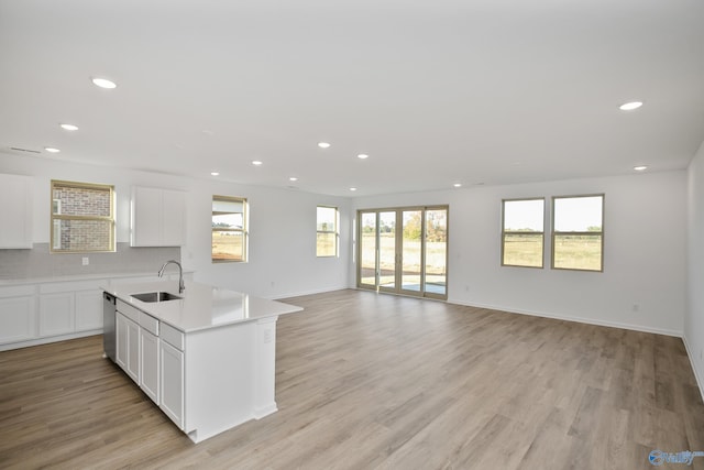 kitchen with sink, light hardwood / wood-style flooring, a kitchen island with sink, backsplash, and white cabinets