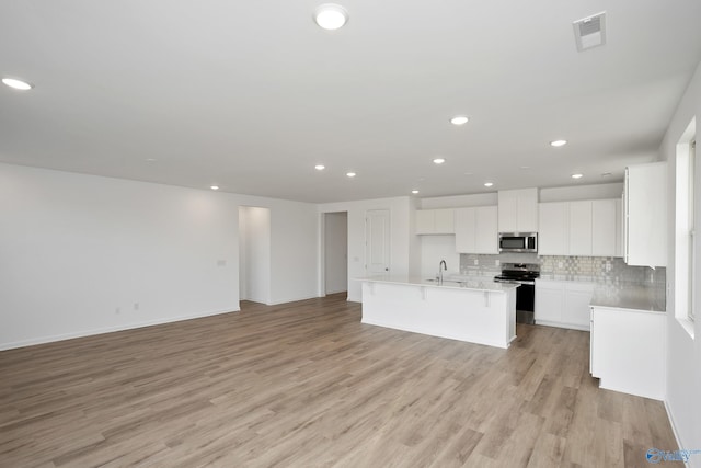 kitchen with appliances with stainless steel finishes, tasteful backsplash, white cabinets, a kitchen island with sink, and light hardwood / wood-style flooring