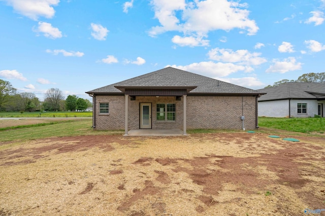 back of property featuring brick siding, a patio area, and roof with shingles